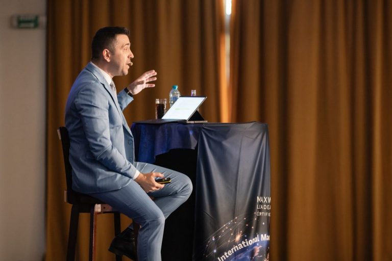 Vorbitor pe scenă, concentrat, în fața publicului la un eveniment Maxwell Leadership România